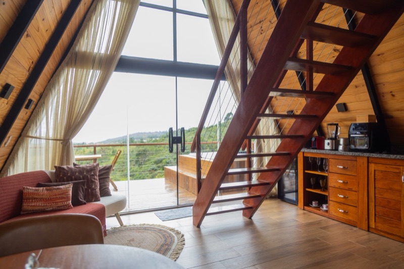 Sala com sofá, escada de madeira e a porta de vidro aberta pro deck