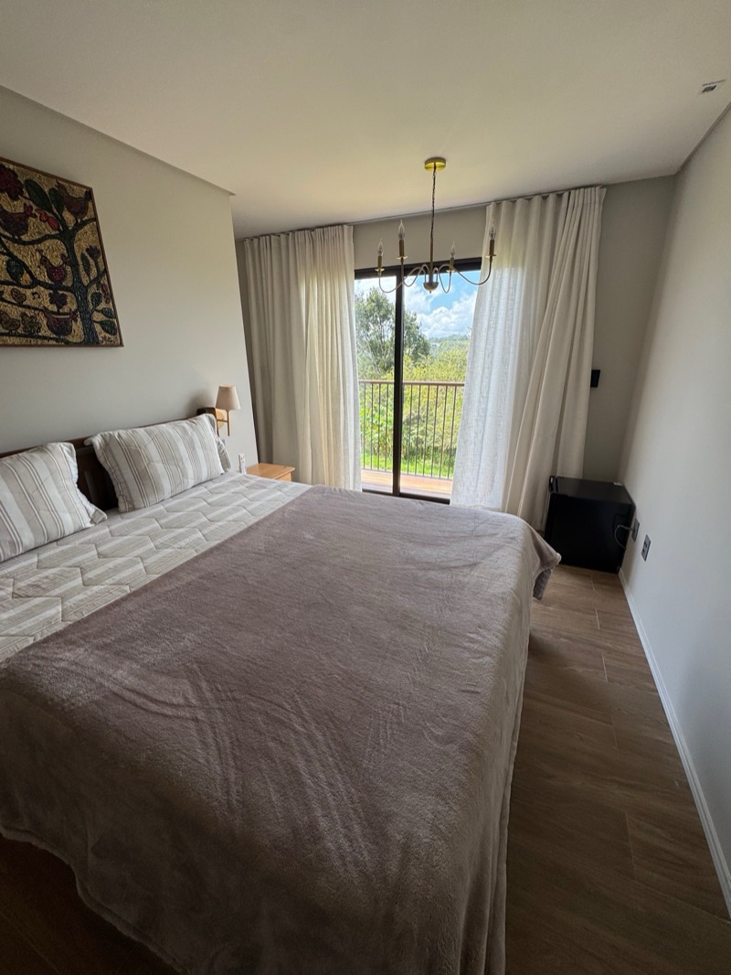 O verde e o deck da varanda vistos pela porta de vidro, com a cama em primeiro plano